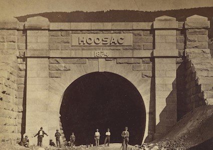 Men stand outside a railroad tunnel. 