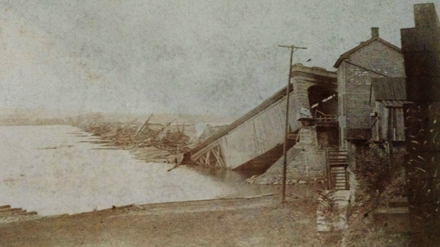A covered wooden bridge is destroyed by wind. Pieces of the wood are sticking out of the water.