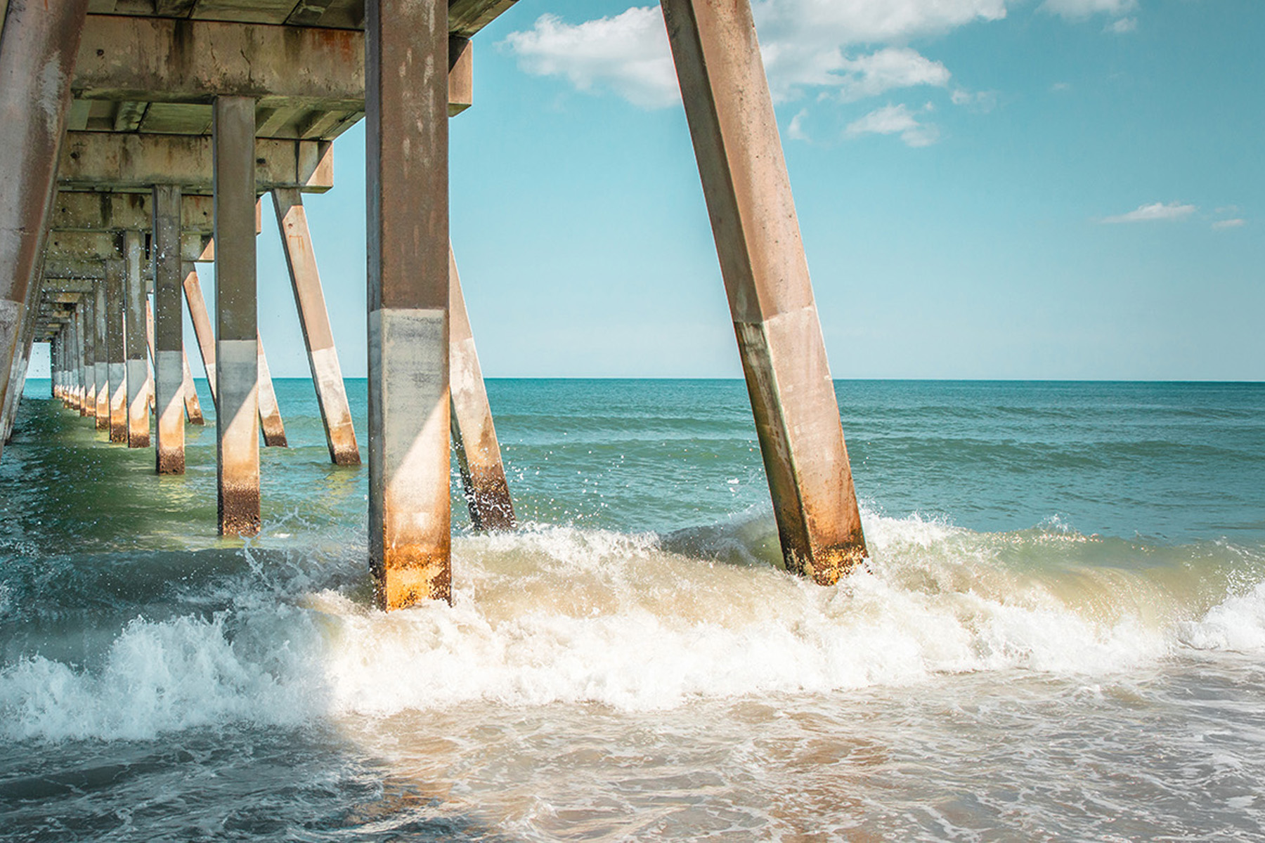 The ocean splashes around concrete piers.