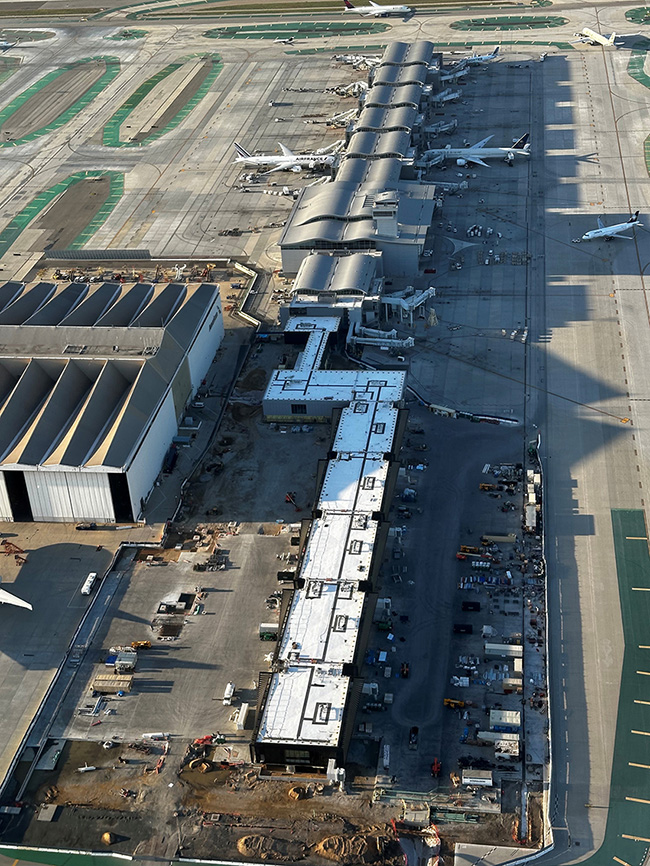 An aerial image shows several white segments connected on the tarmac, which connect to another concourse. 