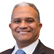 Man in blue jacket, white shirt, and white polka dot tie smiles at the camera. 