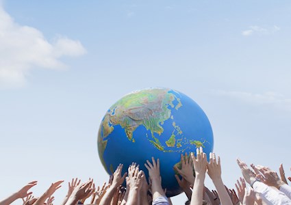 Hands hold up a ball that has the continents on it. 