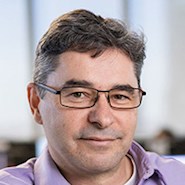 Man wearing glasses and a pink shirt smiles at the camera.